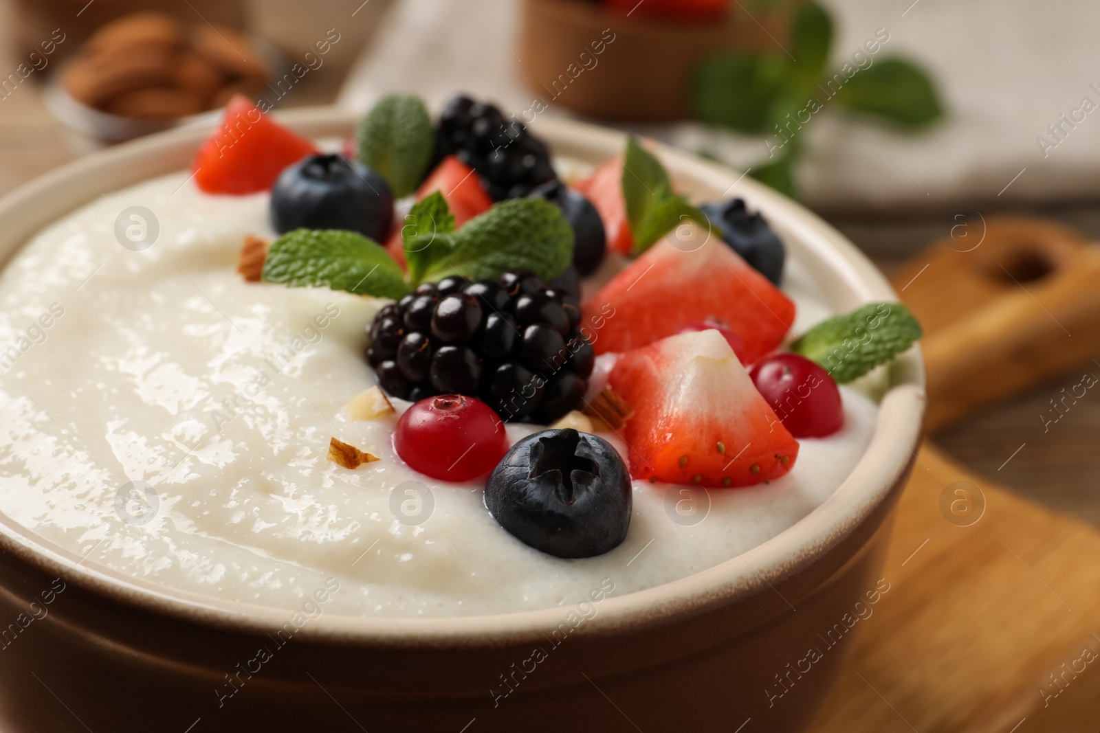 Photo of Delicious semolina pudding with berries in bowl on table, closeup