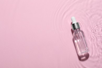 Photo of Bottle of cosmetic oil in water on pink background, top view. Space for text