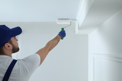 Photo of Handyman painting ceiling with white dye indoors, back view. Space for text