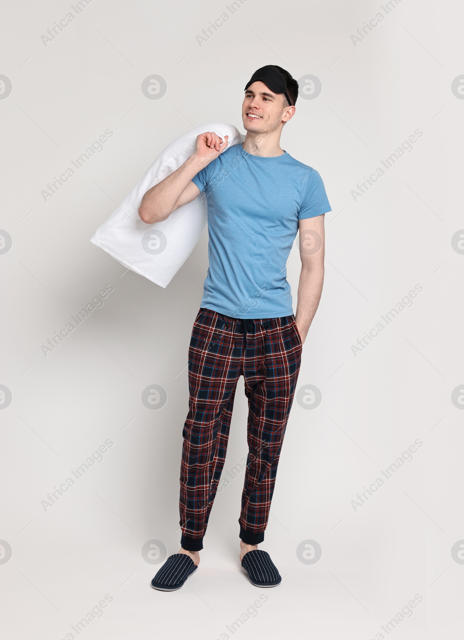 Photo of Happy man in pyjama and sleep mask holding pillow on light grey background