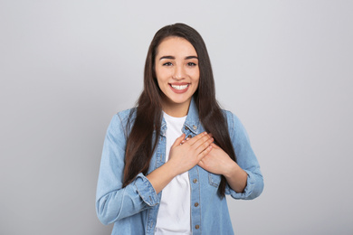 Beautiful grateful woman with hands on chest against light grey background