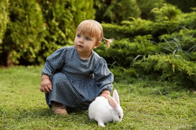 Cute little girl with adorable rabbit on green grass outdoors