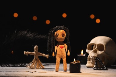 Female voodoo doll with pin in heart and ceremonial items on wooden table against blurred background