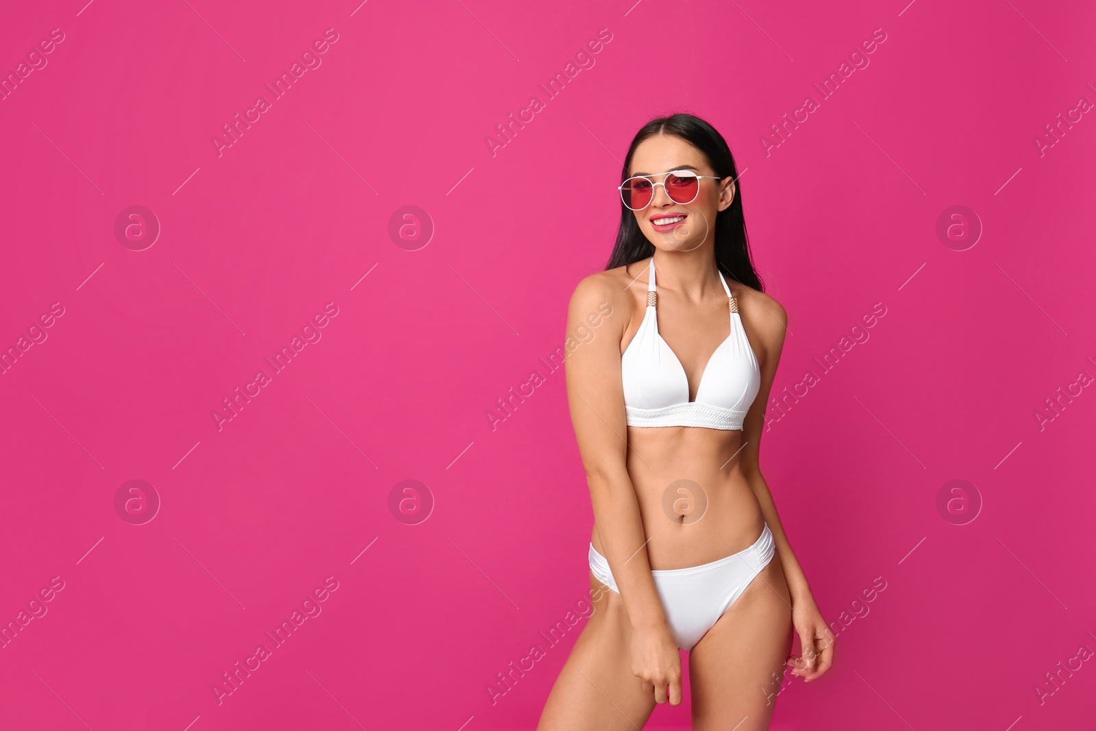 Photo of Beautiful young woman in white bikini with sunglasses on pink background. Space for text