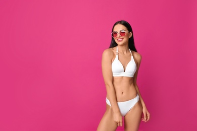 Photo of Beautiful young woman in white bikini with sunglasses on pink background. Space for text