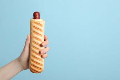 Photo of Woman holding delicious french hot dog on light blue background, closeup. Space for text