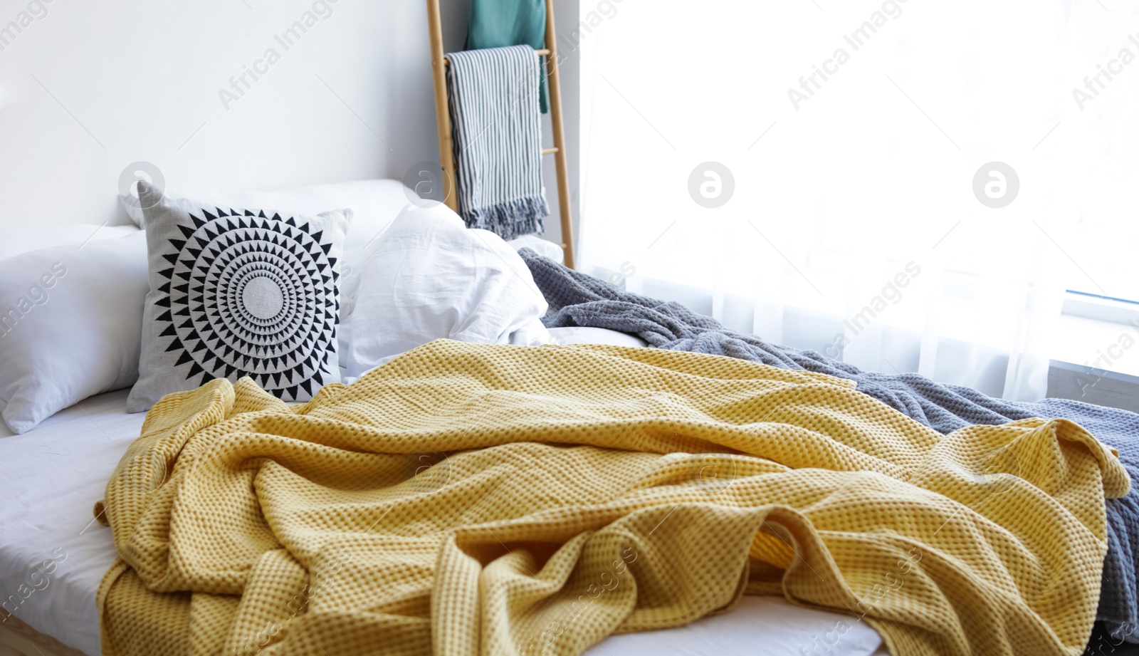 Image of Comfortable bed with yellow blanket and pillows in room. Interior design