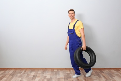 Photo of Male mechanic with car tire on light wall background
