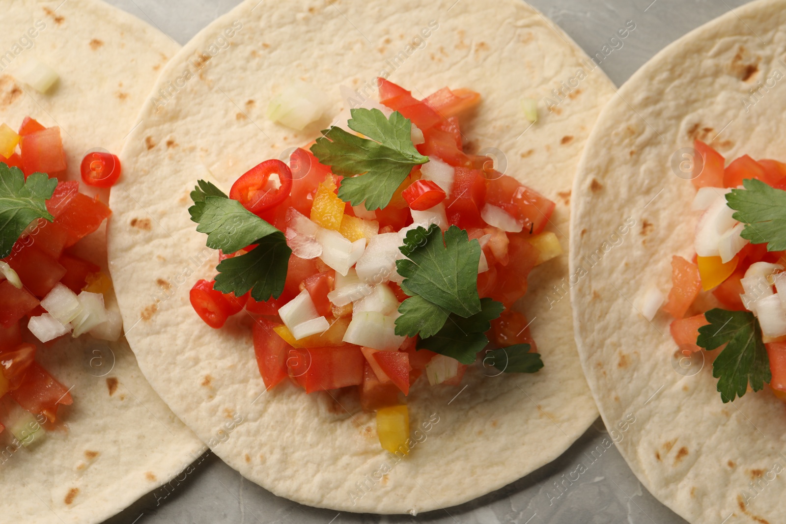 Photo of Delicious tacos with vegetables and parsley on grey table, top view