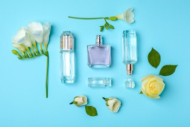 Bottles of perfume and flowers on color background, top view