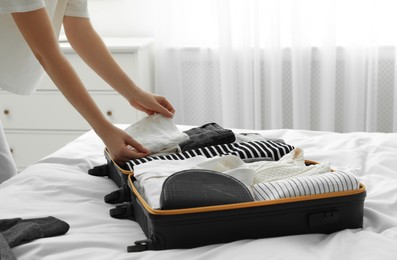 Photo of Woman packing suitcase for trip in bedroom, closeup