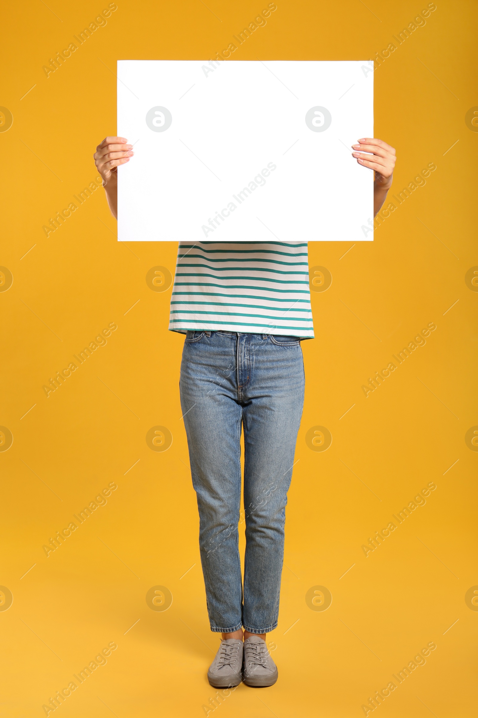 Photo of Woman holding white blank poster on yellow background. Mockup for design