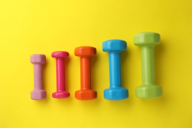 Photo of Many different stylish dumbbells on yellow background, flat lay