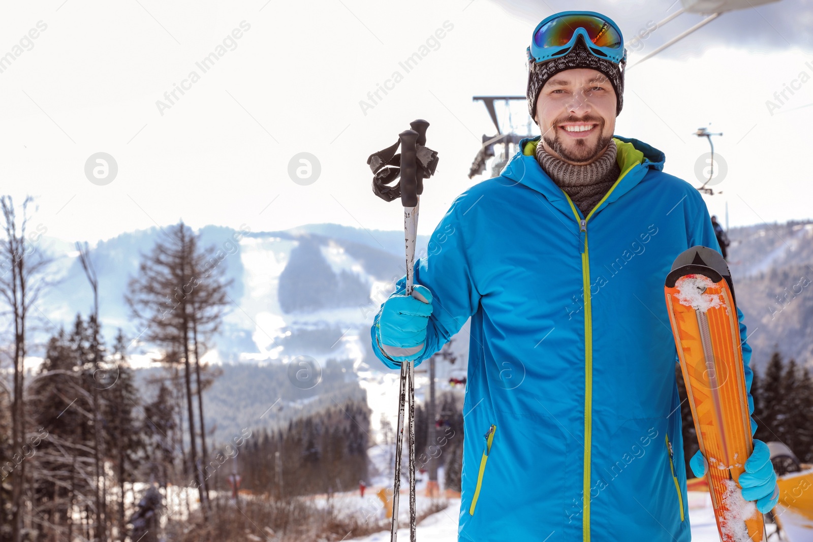 Photo of Happy man with ski equipment near chairlift at mountain resort, space for text. Winter vacation