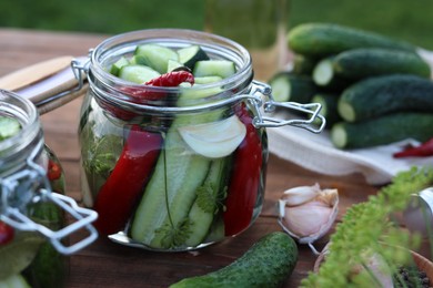 Glass jars with fresh cucumbers and other ingredients on wooden table, closeup. Canning vegetables