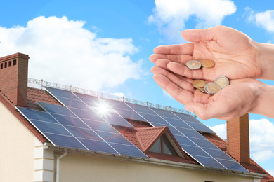 Man holding coins against house with installed solar panels. Renewable energy and money saving