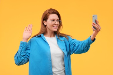 Photo of Beautiful woman in eyeglasses taking selfie on orange background