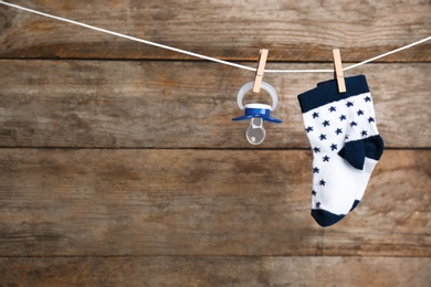 Photo of Pair of socks and pacifier on laundry line against wooden background, space for text. Baby accessories