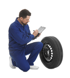 Photo of Professional auto mechanic with wheel and clipboard on white background