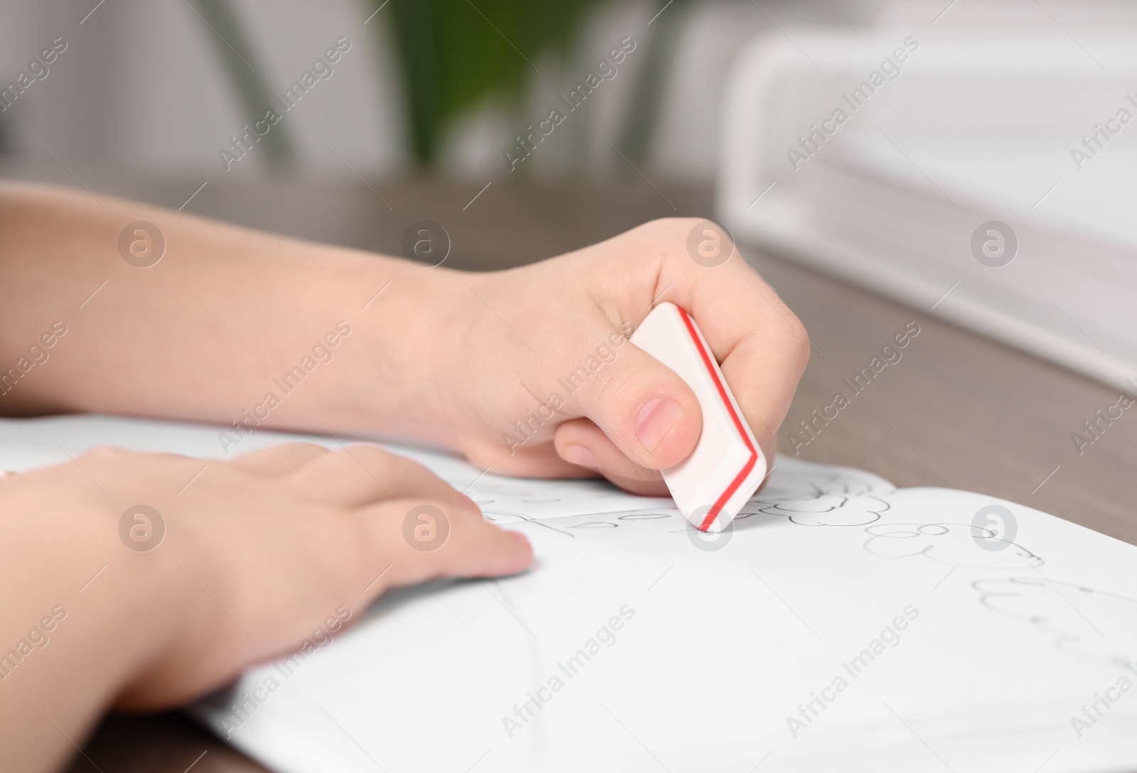 Photo of Girl erasing drawing in her book at wooden table indoors, closeup