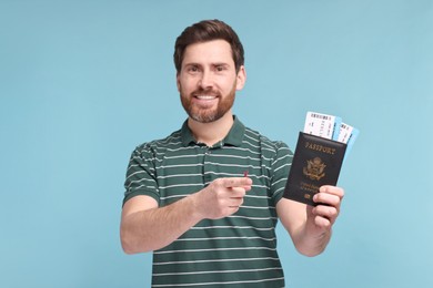 Photo of Smiling man pointing at passport and tickets on light blue background