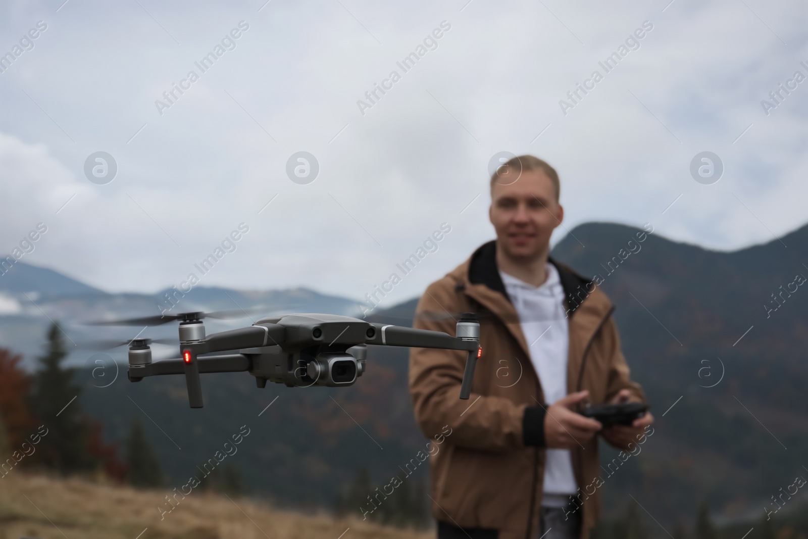 Photo of Young man operating modern drone with remote control in mountains