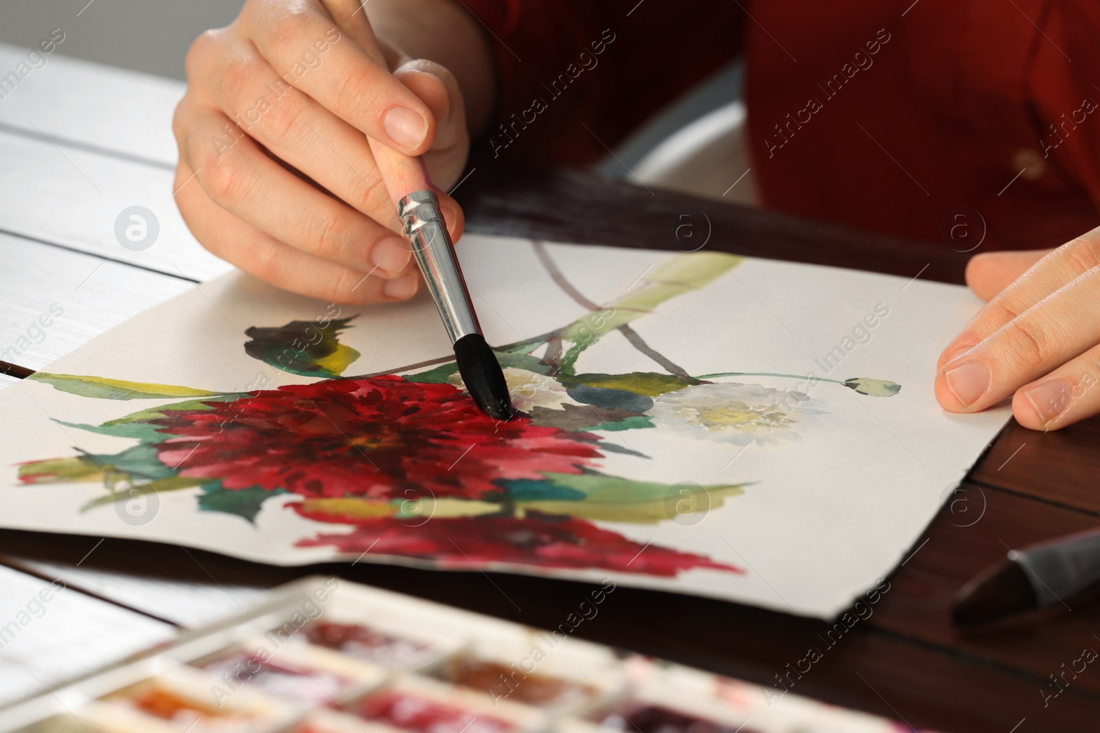 Photo of Woman painting flowers with watercolor at wooden table, closeup. Creative artwork