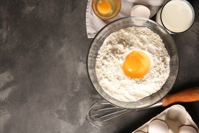 Photo of Making dough. Flour with egg yolk in bowl and other products on grey textured table, flat lay. Space for text