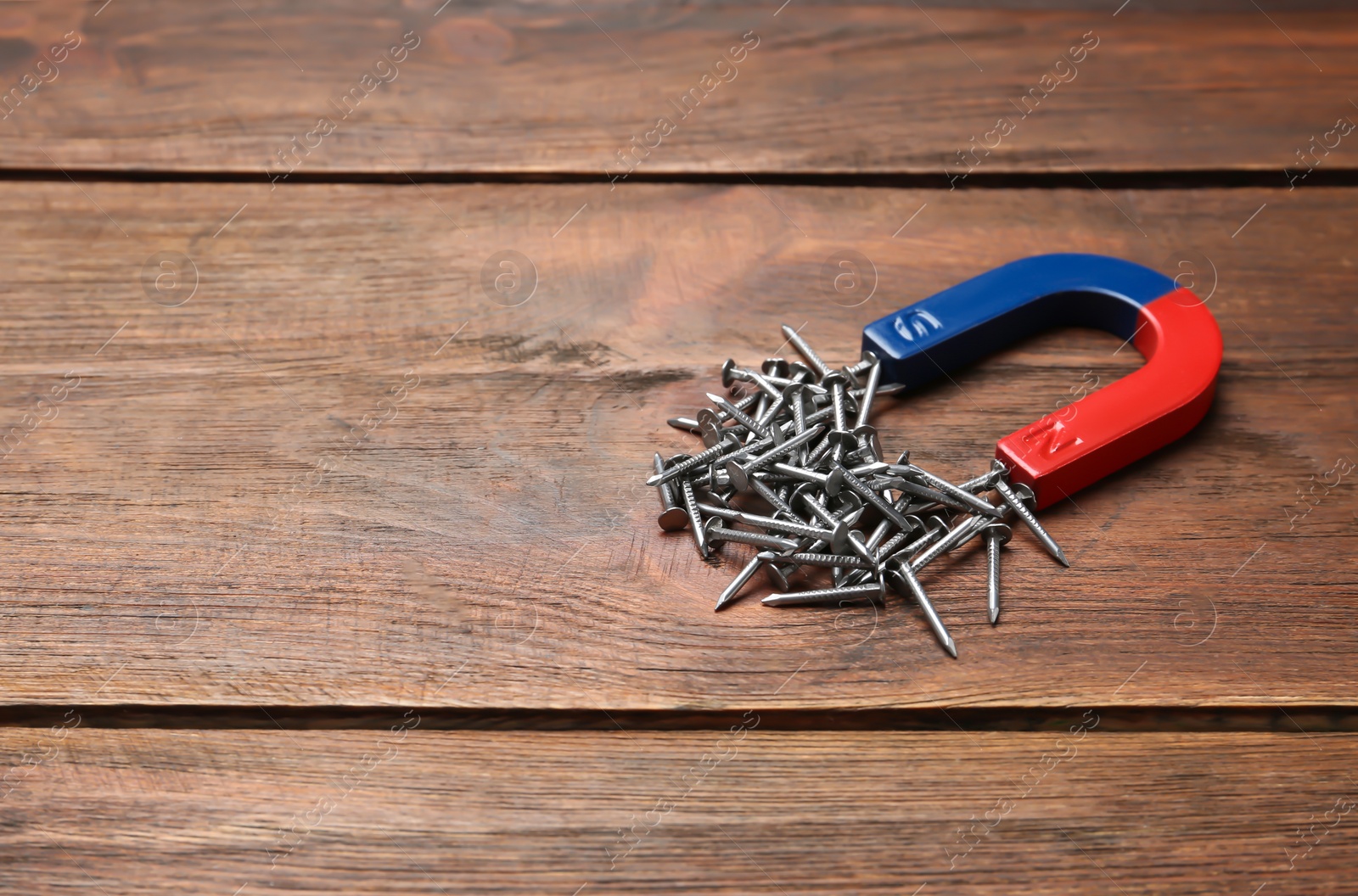 Photo of Magnet attracting nails on wooden background, space for text