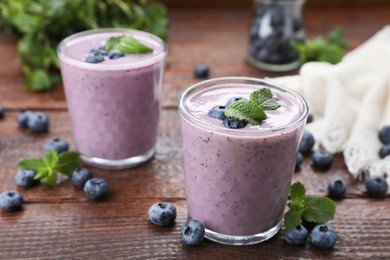 Photo of Glasses of blueberry smoothie with fresh berries and mint on wooden table, closeup