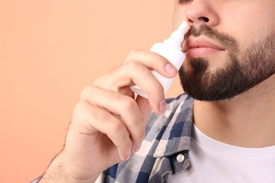 Man using nasal spray on peach background, closeup. Space for text