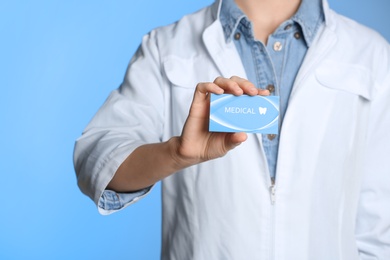 Photo of Doctor holding business card on color background, closeup with space for text. Dental medical service