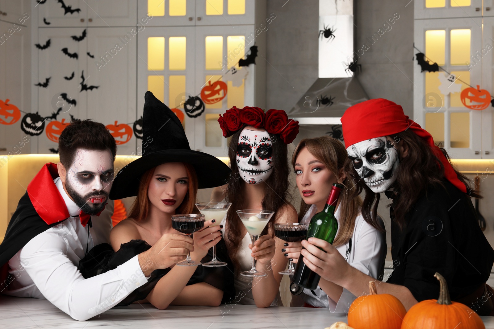 Photo of Group of people in scary costumes with cocktails celebrating Halloween indoors