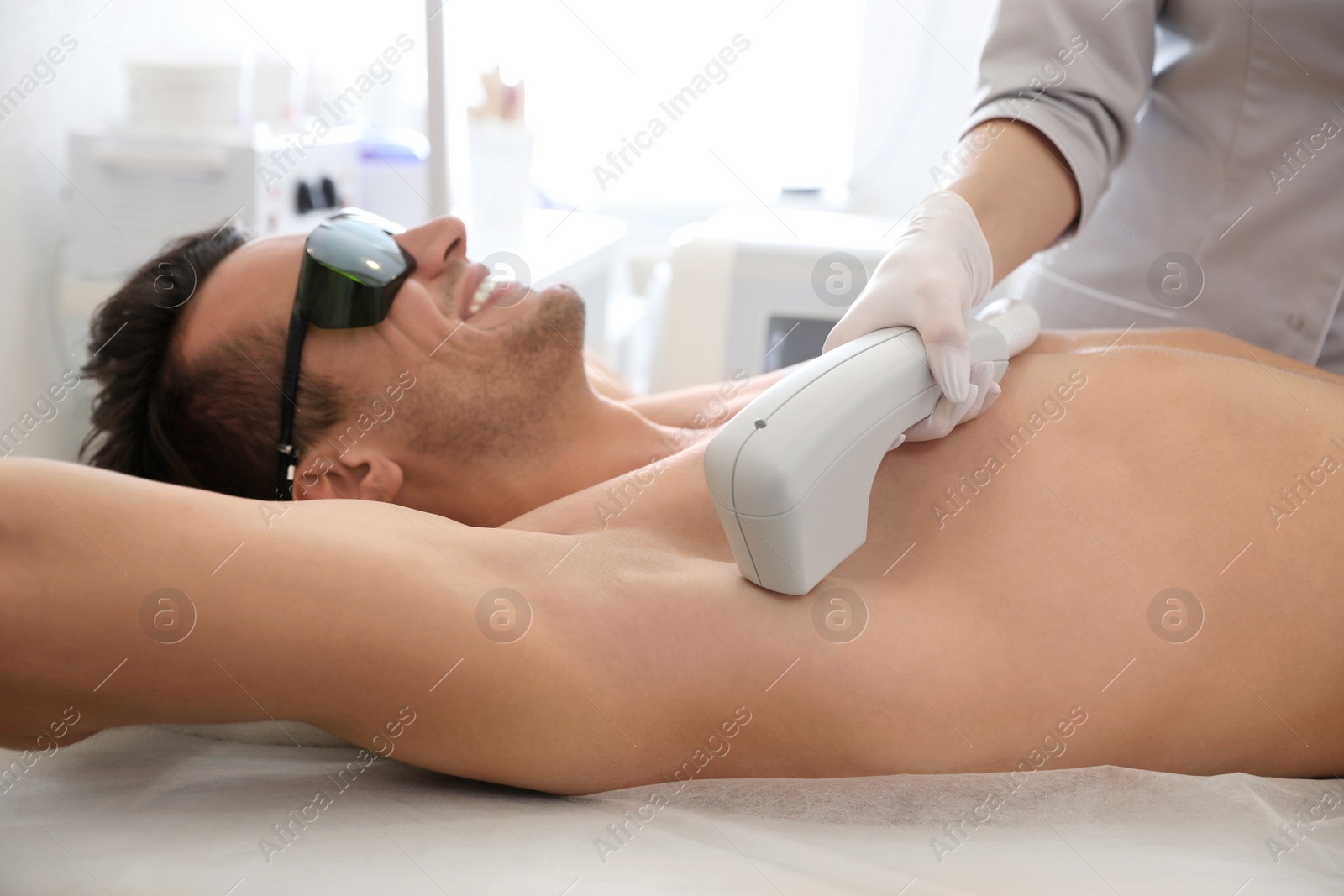 Photo of Young man undergoing laser epilation procedure in beauty salon