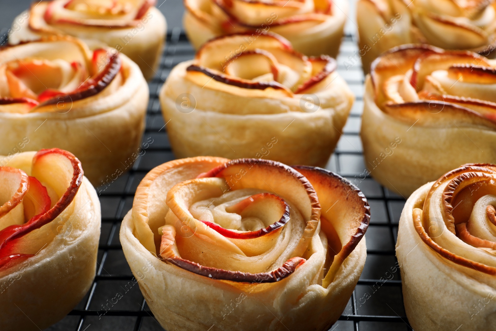 Photo of Cooling rack with freshly baked apple roses on grey table, closeup. Beautiful dessert