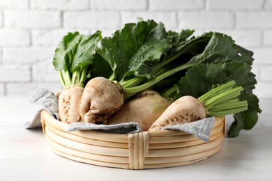 Photo of Basket with fresh sugar beets on white table near brick wall