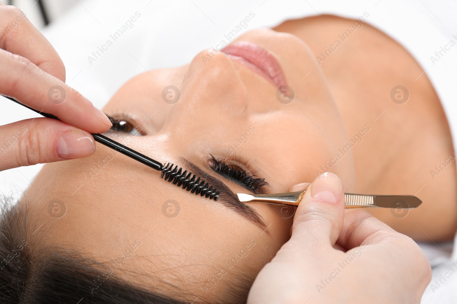 Photo of Young woman having professional eyebrow correction procedure in beauty salon