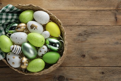 Photo of Many beautifully decorated Easter eggs in wicker basket on wooden table, top view. Space for text