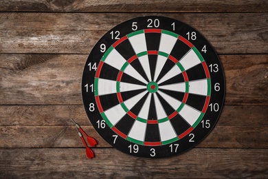 Dart board with color arrows on wooden background, top view. Space for text