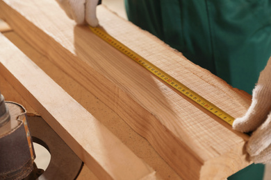 Professional carpenter measuring wooden board at workbench, closeup