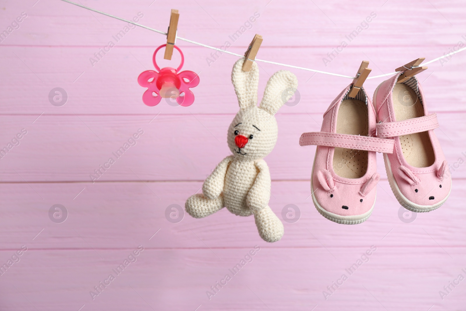 Photo of Pair of shoes, pacifier and toy bunny on laundry line against wooden background. Baby accessories