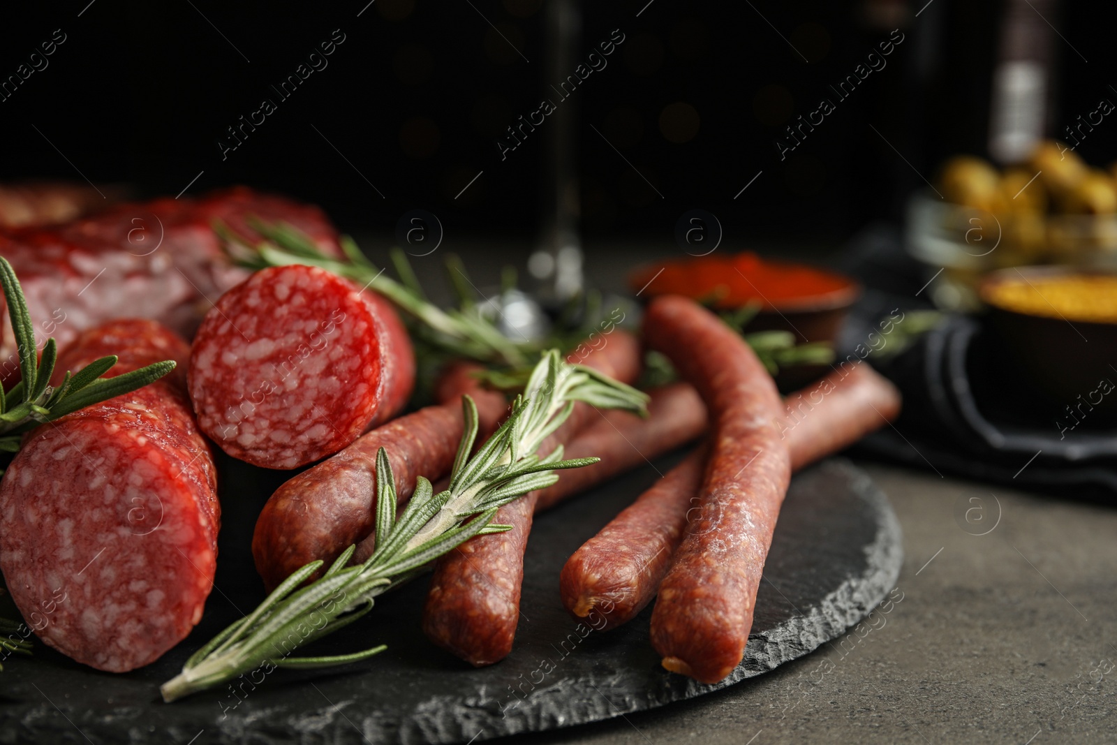 Photo of Different types of sausages with rosemary on grey table, closeup