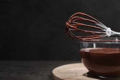 Bowl of chocolate cream and whisk on gray table, space for text