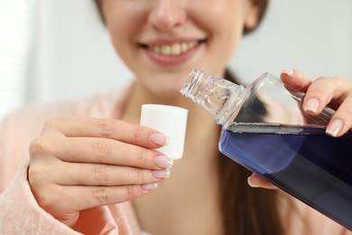 Young woman using mouthwash on blurred background, closeup