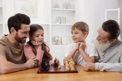 Photo of Family playing chess together at table in room