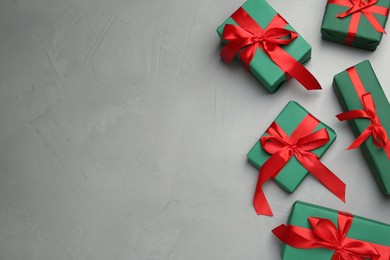 Photo of Many green gift boxes with red bows on light grey table, flat lay. Space for text