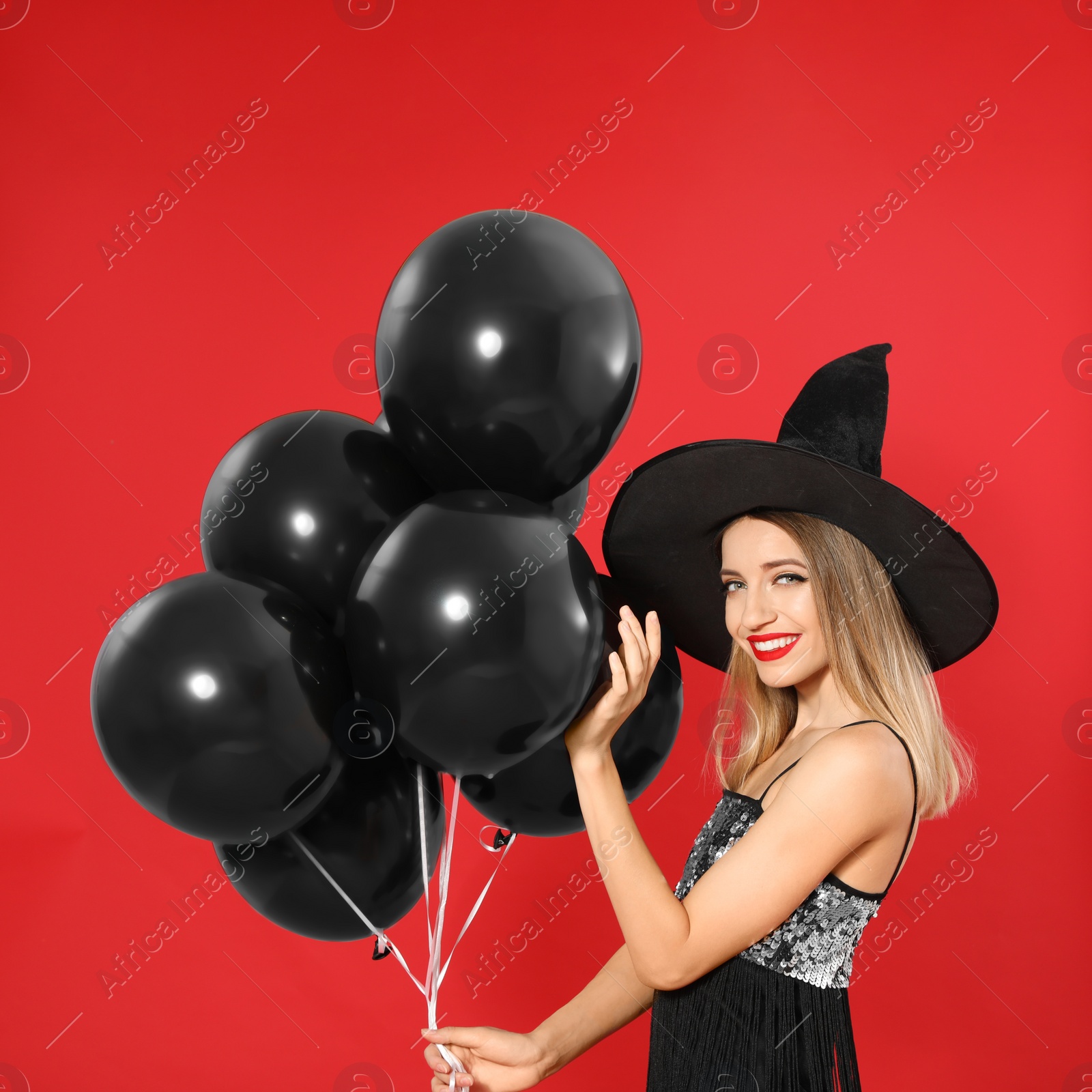 Photo of Beautiful woman wearing witch costume with balloons for Halloween party on red background