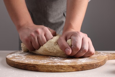 Photo of Man kneading dough at table near grey wall, closeup