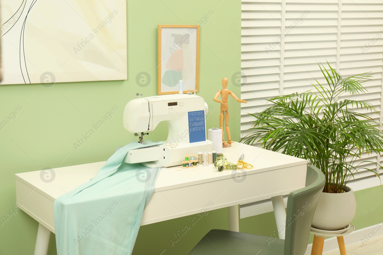 Photo of Modern sewing machine with cloth and craft accessories on white table near window in room