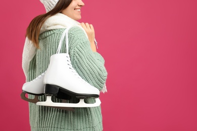 Photo of Happy woman with ice skates on pink background, closeup. Space for text